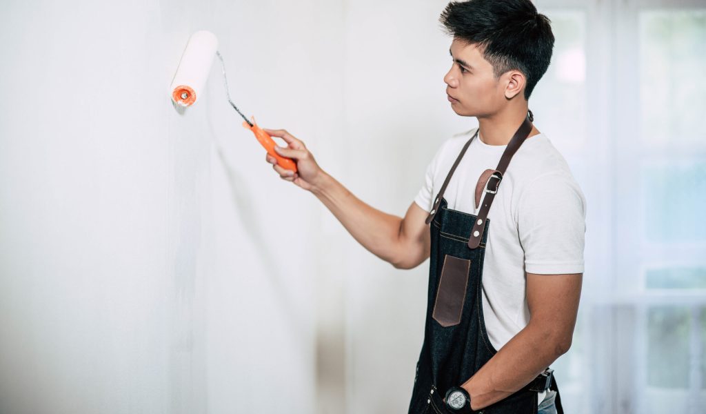 A carpenter holds a paintbrush and paints wood. Selective focus.