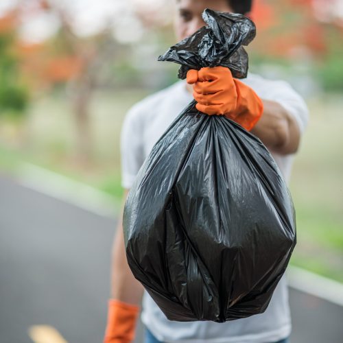 A man wearing orange gloves collecting garbage in a black bag. Selective focus.